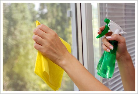 Person cleaning a window with a green spray bottle and yellow rag